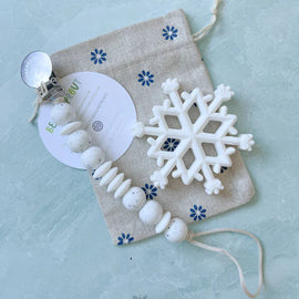 White snowflake silicone baby teether with matching speckled white pacifier clip from Bead Sprout, styled on a fabric pouch.