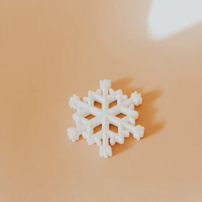 Close-up of white snowflake silicone teether placed on a warm beige background.