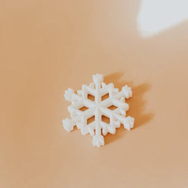 Close-up of white snowflake silicone teether placed on a warm beige background.