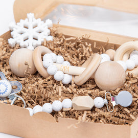 Baby gift set with wooden rattle, silicone bead pacifier clip, snowflake teether, and sensory teething ring in a kraft box with crinkle paper.