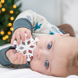 Baby holding a snowflake toy with a blurred Christmas tree in the background