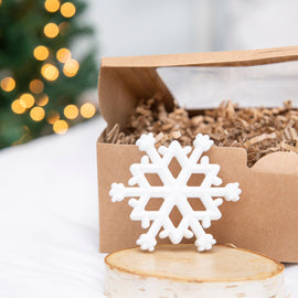 White snowflake teether on a wooden surface with a blurred Christmas tree in the background