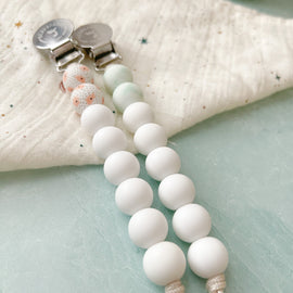 Classic silicone bead pacifier clips with vintage-inspired designs and stainless steel clips on a soft muslin cloth. 