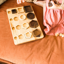 Child playing with wooden geometric puzzle pieces on soft couch, Montessori wooden shape stacking toy.