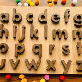 Wooden alphabet board with vintage walnut lowercase letters surrounded by colorful pom poms, Montessori early literacy puzzle.