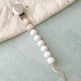 Poppy flower white silicone pacifier clips with stainless steel clip displayed on fabric. 