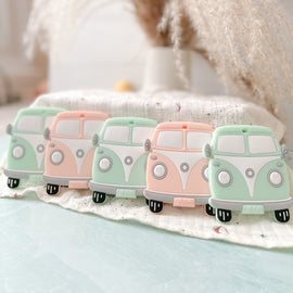 set of vintage van silicone baby teethers in mint and peach color displayed on a soft cloth. 